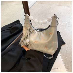 Detail of grey satin baguette bag featuring floral embroidery and clear beaded handle