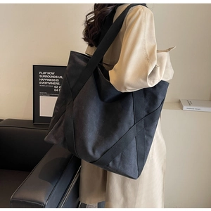 Spacious black canvas tote bag shown worn over the shoulder with minimalist trench coat