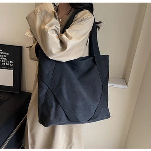 Detail of a large black canvas tote bag with wide straps worn by a model in a trench coat