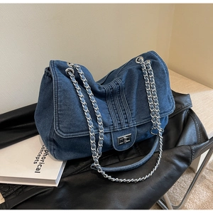 Détail du sac bandoulière en denim bleu avec chaîne argentée et fermoir pivotant en métal