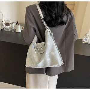 Sac fourre-tout argenté métallisé avec nœud porté à l'épaule dans un café minimaliste