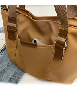 Detail of tan canvas tote bag front pocket showing phone storage and reinforced stitching