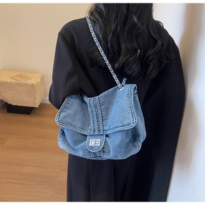 Détail du sac cabas en denim bleu avec bandoulière en chaîne et fermoir rotatif argenté