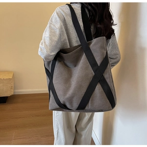 Detail of a large dark grey canvas tote bag with black webbing straps shown on a model