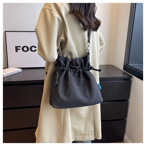 Détail du sac seau noir en toile avec cordon de serrage, étiquette et poche frontale