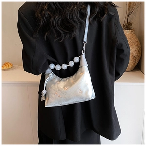 Detail of silver satin baguette bag featuring floral embroidery and marble bead strap