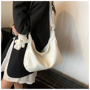 Détail d'un sac bandoulière blanc plissé avec une breloque d'ours en peluche