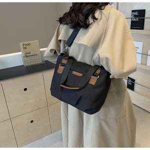 Black canvas tote bag with brown leather handles and adjustable shoulder strap shown on model