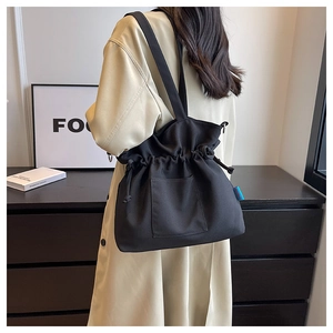 Détail du grand sac cabas plissé noir avec cordon et étiquette bleue porté par un mannequin