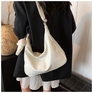 Vue latérale du sac hobo crème avec bandoulière large et charm en peluche dans un salon