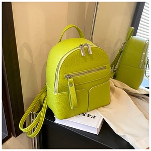 Detail of neon green mini backpack in lychee leather showing front zip and side pockets