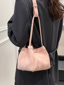 Borsa a secchiello rosa lucida plissettata con borchie sopra un blazer nero