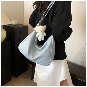 Détail d'un sac hobo bleu clair en cuir litchi avec un pendentif ours blanc en peluche