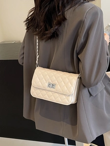 Beige gesteppte Umhängetasche mit Silberkette an Model in grauem Blazer getragen