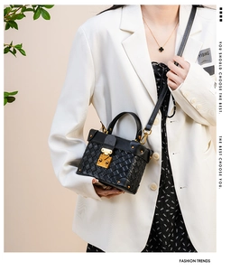 Detail of black woven bucket bag with gold hardware worn by a model in a white suit