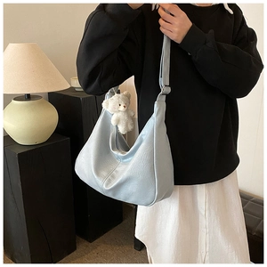 Détail du sac croissant bleu clair avec texture cuir et breloque ours en peluche
