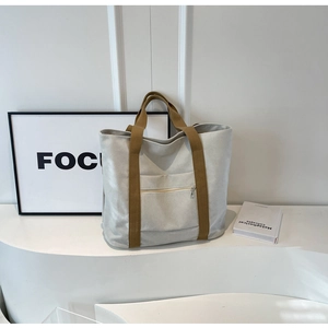 Detail view of canvas tote bag with front zipper pocket and brown fabric handles