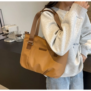 Detail of khaki nylon tote bag with front zipper pocket and webbing shoulder strap on model