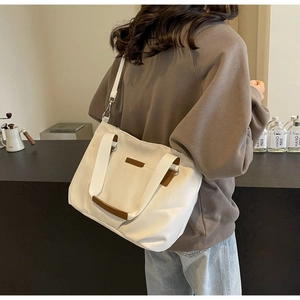 Detail of white canvas tote bag with brown leather handles and adjustable shoulder strap