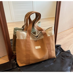 Detail of contrast color canvas tote bag showing wide straps and brand label on a wooden floor