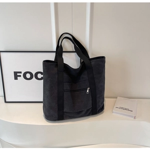 Detail of black canvas tote bag showing the functional front zipper pocket and wide strap