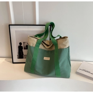 Detail view of large canvas tote bag with green contrast straps and leather brand tag