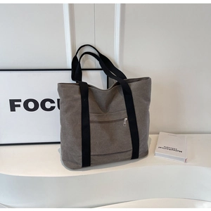 Close-up of grey canvas tote bag featuring durable black straps and front zipper pocket