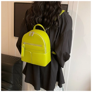 Detail view of mini neon yellow textured leather backpack worn by model in black outfit