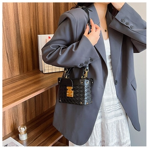 Detail of a quilted black leather trunk bag with gold hardware worn by a model