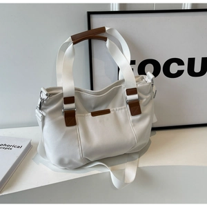Close-up of white canvas tote bag with brown leather handles and adjustable shoulder strap