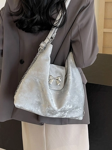Sac tote en velours argenté avec nœud métallique et bandoulière en chaîne porté à l'épaule