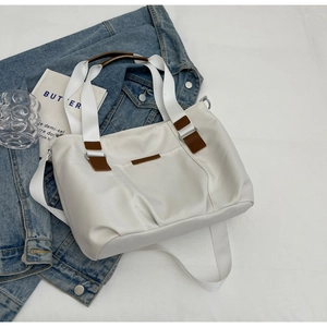 Detail of a large white nylon tote bag with brown leather accents on a denim jacket