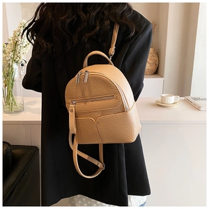 Close-up of beige mini leather backpack with lychee texture and dual zippers on a model