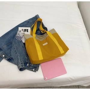 Flat lay detail of mustard canvas tote bag with beige trim and white woven label