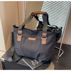 Close-up of black canvas tote with brown leather handles and adjustable woven strap