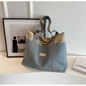 Detail of grey-blue and beige canvas tote bag showing contrast stitching and logo tag
