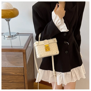 Detail of a white quilted box bag with a gold metal lock and adjustable shoulder strap