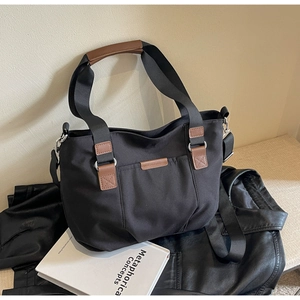 Detail of a black canvas tote bag with brown handles and a detachable shoulder strap
