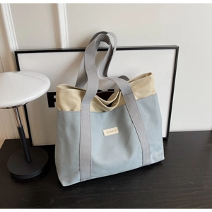 Detail of blue and beige canvas tote bag with leather logo patch and grey straps