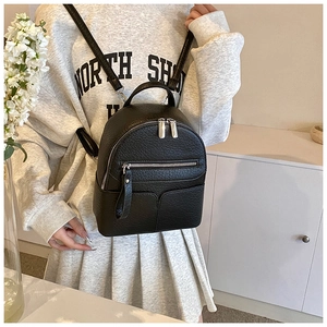Close-up of a mini black leather backpack featuring pebbled texture and silver zippers