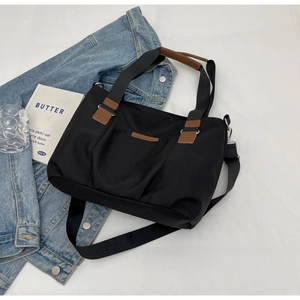 Detail of black nylon tote bag with brown leather accents and adjustable shoulder strap