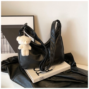 Détail du sac à bandoulière en cuir noir avec un porte-clé ours en peluche blanc et texture douce