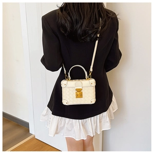 Close-up of white leather box bag with gold metal push-lock and quilted diamond pattern