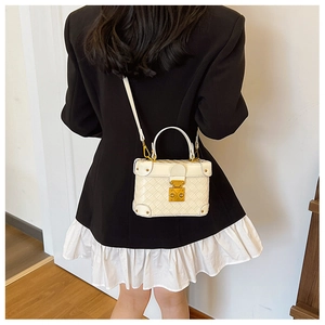 Detail of white quilted trunk bag with gold metal corners and vintage clasp on black dress