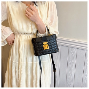 Detail of black quilted box bag featuring golden hardware and rivets on a crossbody strap