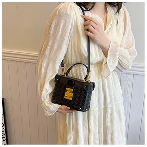 Detail of black woven bucket bag with gold metal lock and adjustable crossbody strap