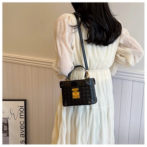 Detail of black woven texture leather handbag with gold clasp and metal corner accents