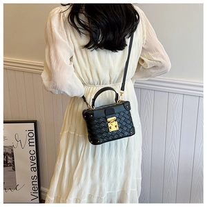 Detail of a black quilted box bucket bag with gold hardware worn with a white dress