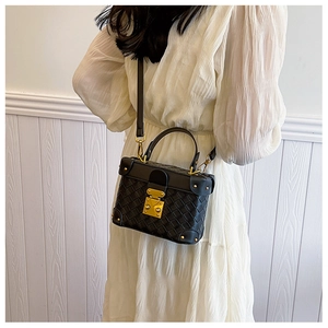 Close-up of black woven box bag featuring premium gold hardware on a white dress