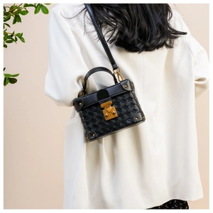 Detail of a black woven leather box bag with gold hardware worn over a white blazer